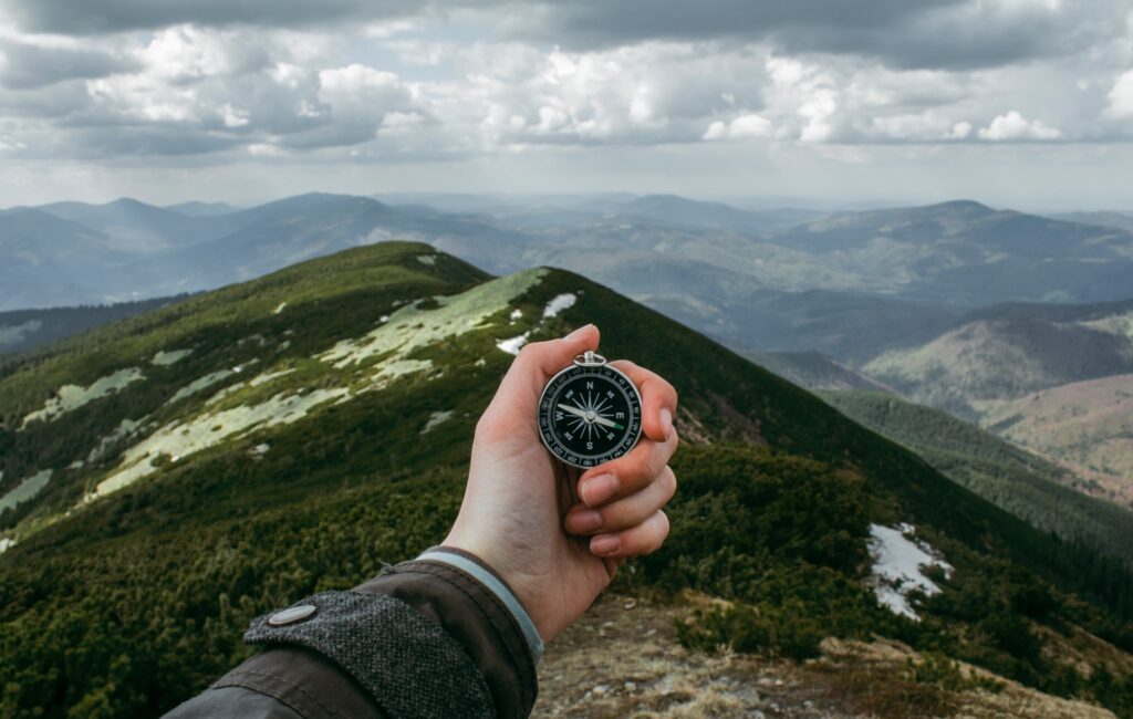 A person holding a compass and standing in front of a mountain
