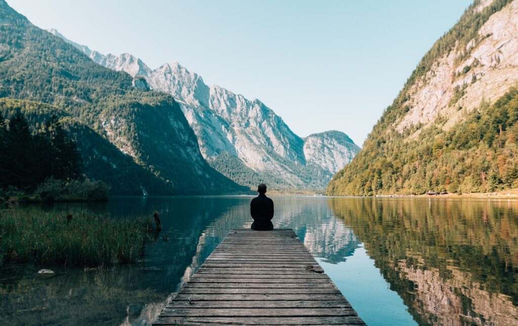 A person sitting at the edge of the pathway to the lake with the mountains ahead