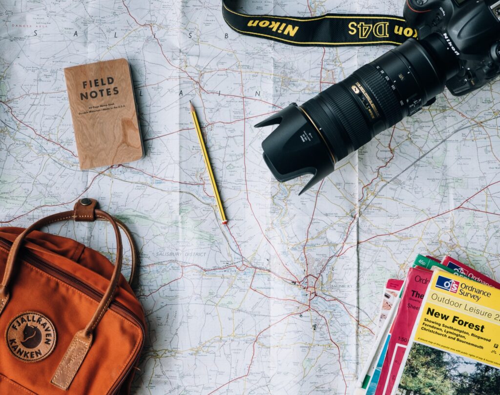 A map, a camera, bag, notebook, a pencil and travel guides all laid out on a map